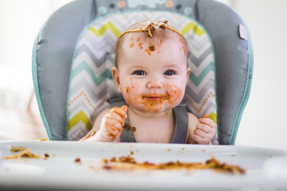 Baby in high chair covered in spaghetti Bolognese