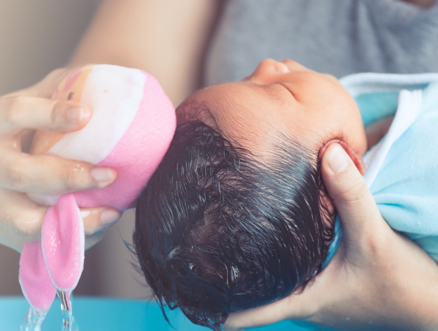Cute asian newborn baby girl take a bath. Mom cleaning her baby hair with sponge