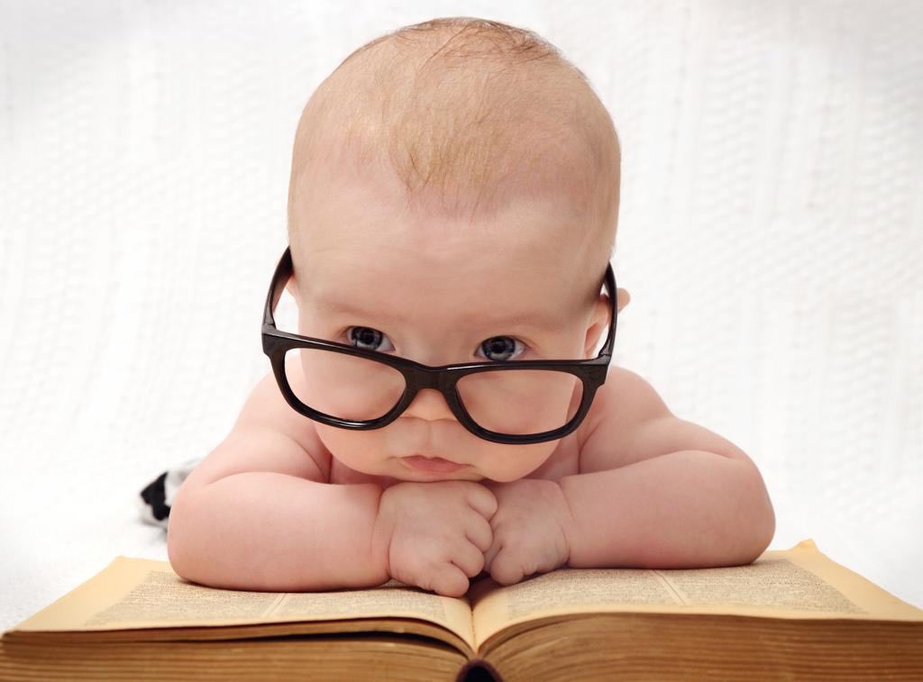 Funny picture of a baby with glasses on lying on a book