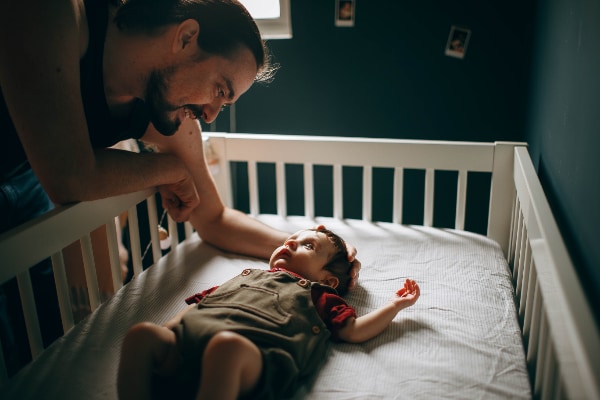 Dad settles toddler in a cot, following a Toddler Sleep Training Plan
