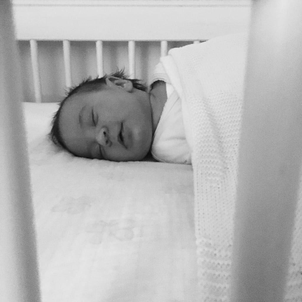 A black and white image of a Baby asleep in a cot